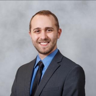 Andrew, dressed in formal attire, smiles at the camera