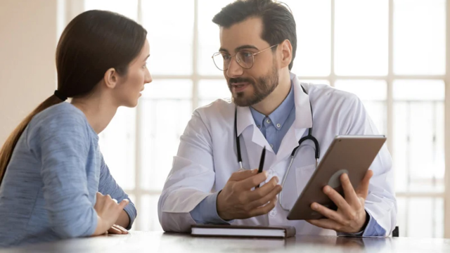 A doctor sits at a table speaking with a patient. 