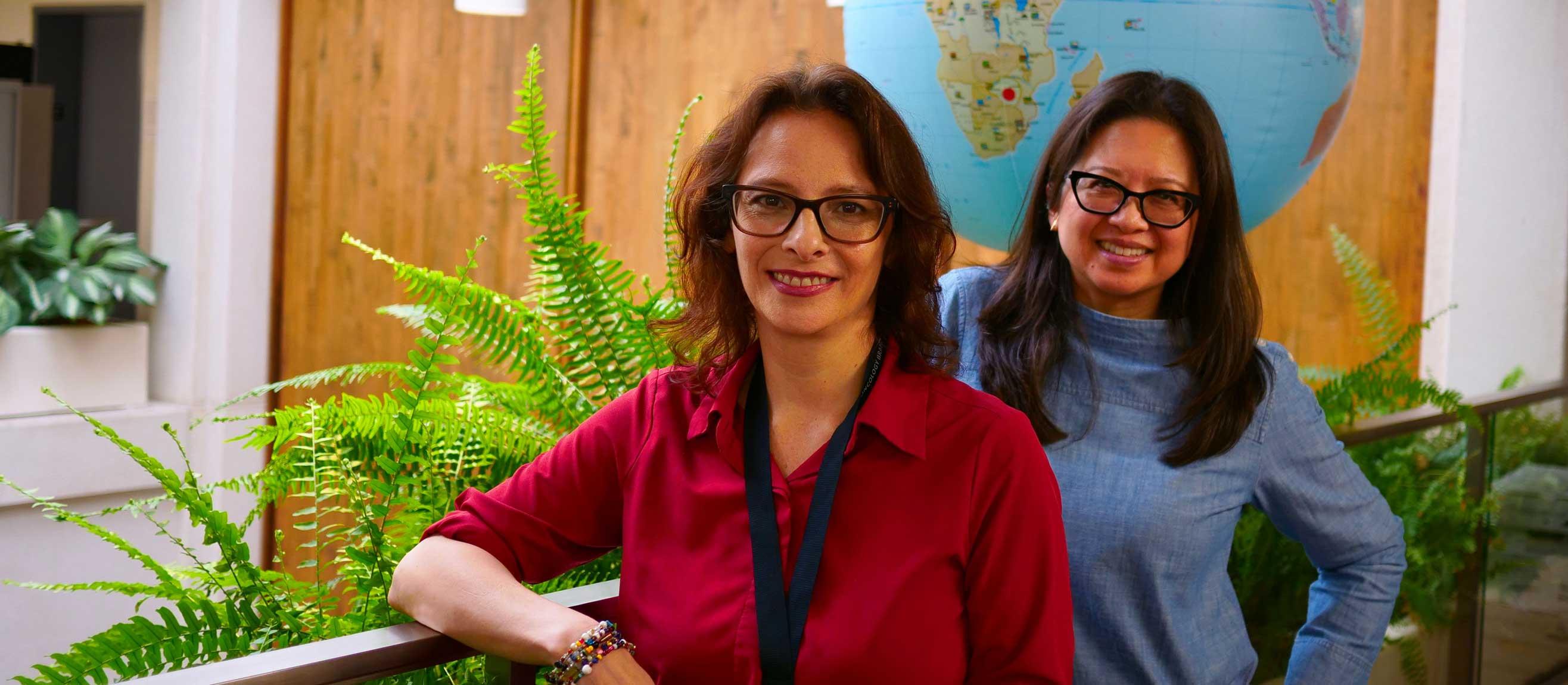 Jennifer Reyes and Claudia Chambers smiling next to each other by an inflatable globe and ferns