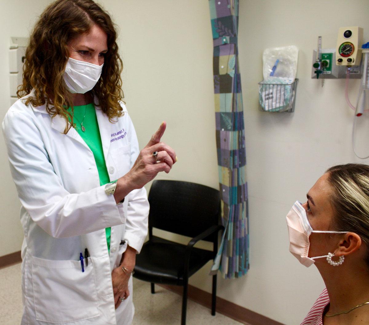 Research Nurse Tricia Kunst in the clinic asking a seated patient to track her finger as part of an exam.