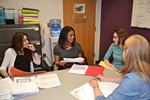 four women sit around a table talking 